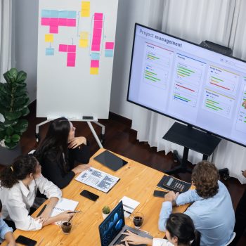 Project manager planning schedules for business task at meeting room, Gantt chart software show on TV screen. Multi ethnic diversity business people and modern business project management. Meticulous