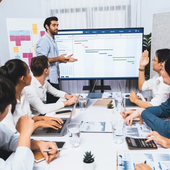 Project manager communicate and collaborate with team using project management software display on monitor, tracking progress of project task and making schedule plan at meeting table. Prudent