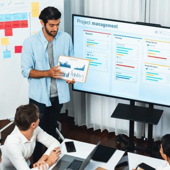 Project manager communicate and collaborate with team using project management software display on monitor, tracking progress of project task and making schedule plan at meeting table. Prudent